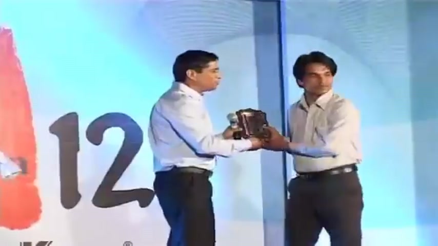 Award presentation on stage at Su-Kam with a senior leader handing a trophy to an employee at a 12-year milestone celebration