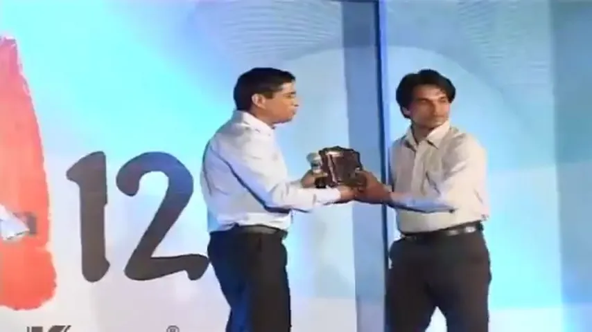Award presentation on stage at Su-Kam with a senior leader handing a trophy to an employee at a 12-year milestone celebration