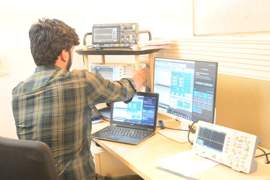 Su-vastika engineer at a lab bench with oscilloscopes and battery monitoring software