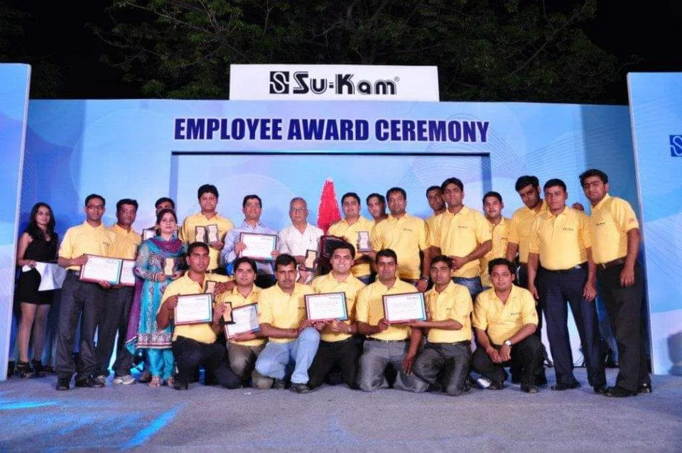 Su-Kam employee award ceremony — staff on stage with certificates under the Su-Kam banner